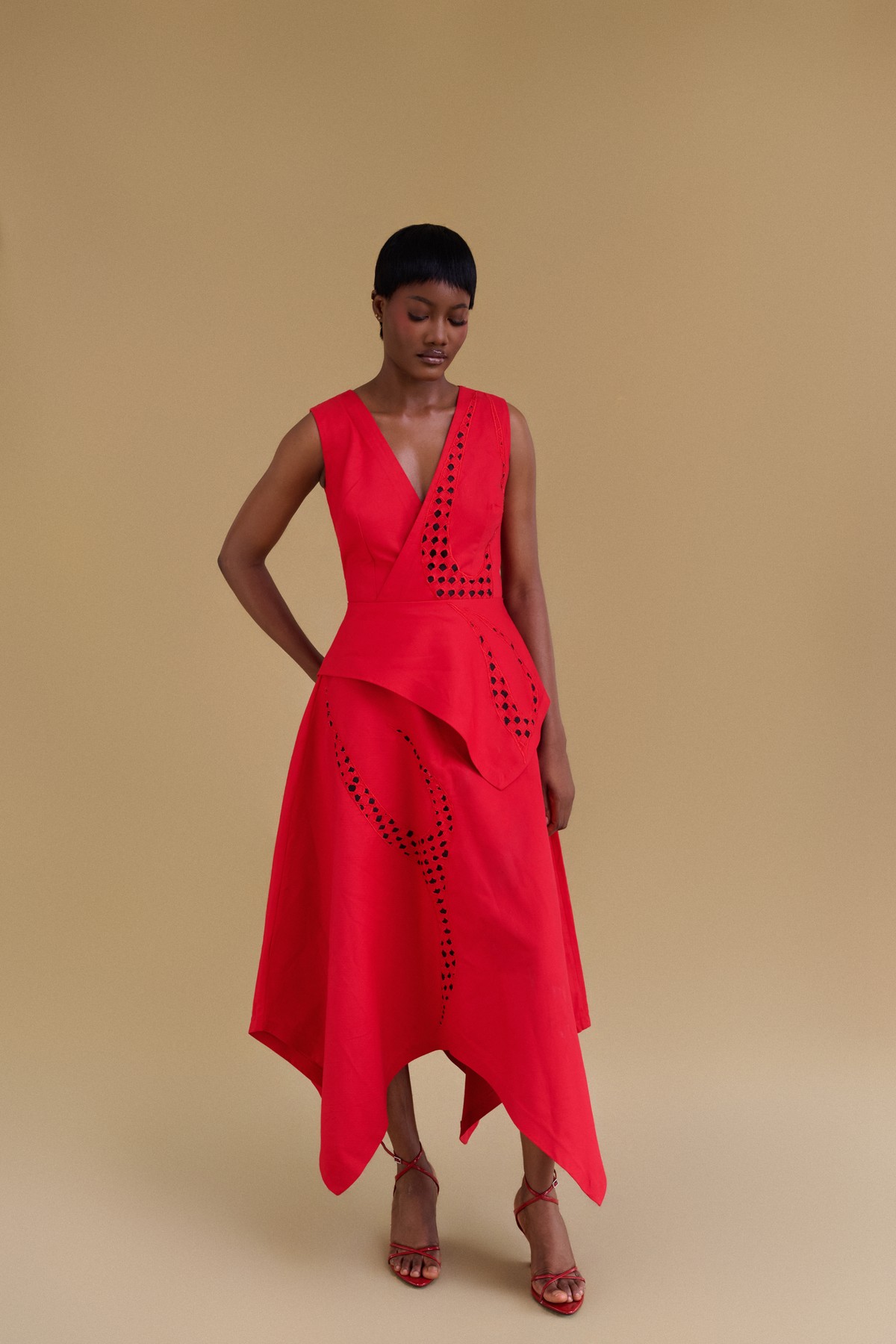 Model wearing a bright red skirt with geometric cutout details, standing against a solid beige studio background.