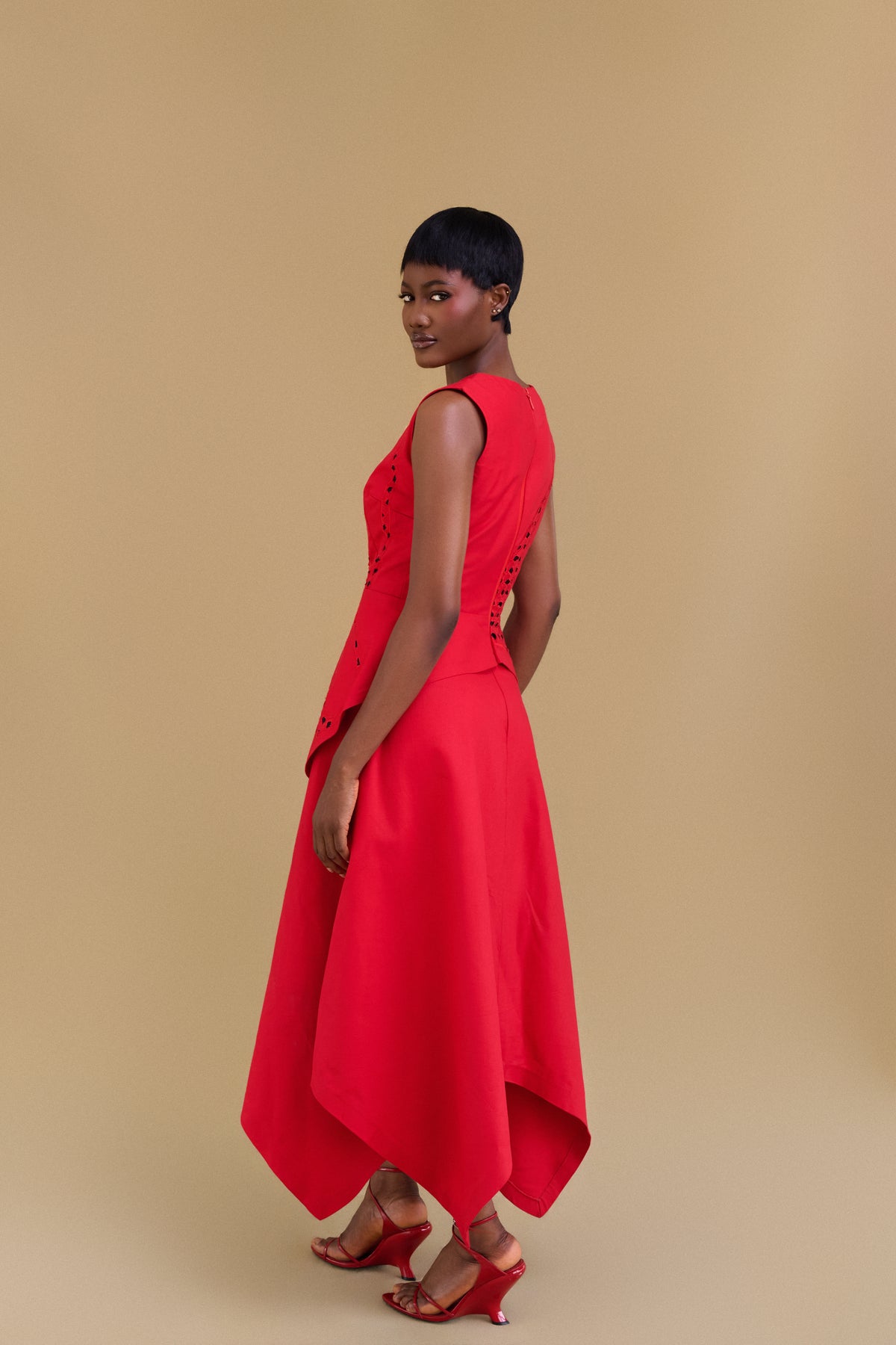 Vibrant red skirt with asymmetric hem,  side view on a model standing against a solid beige studio background.